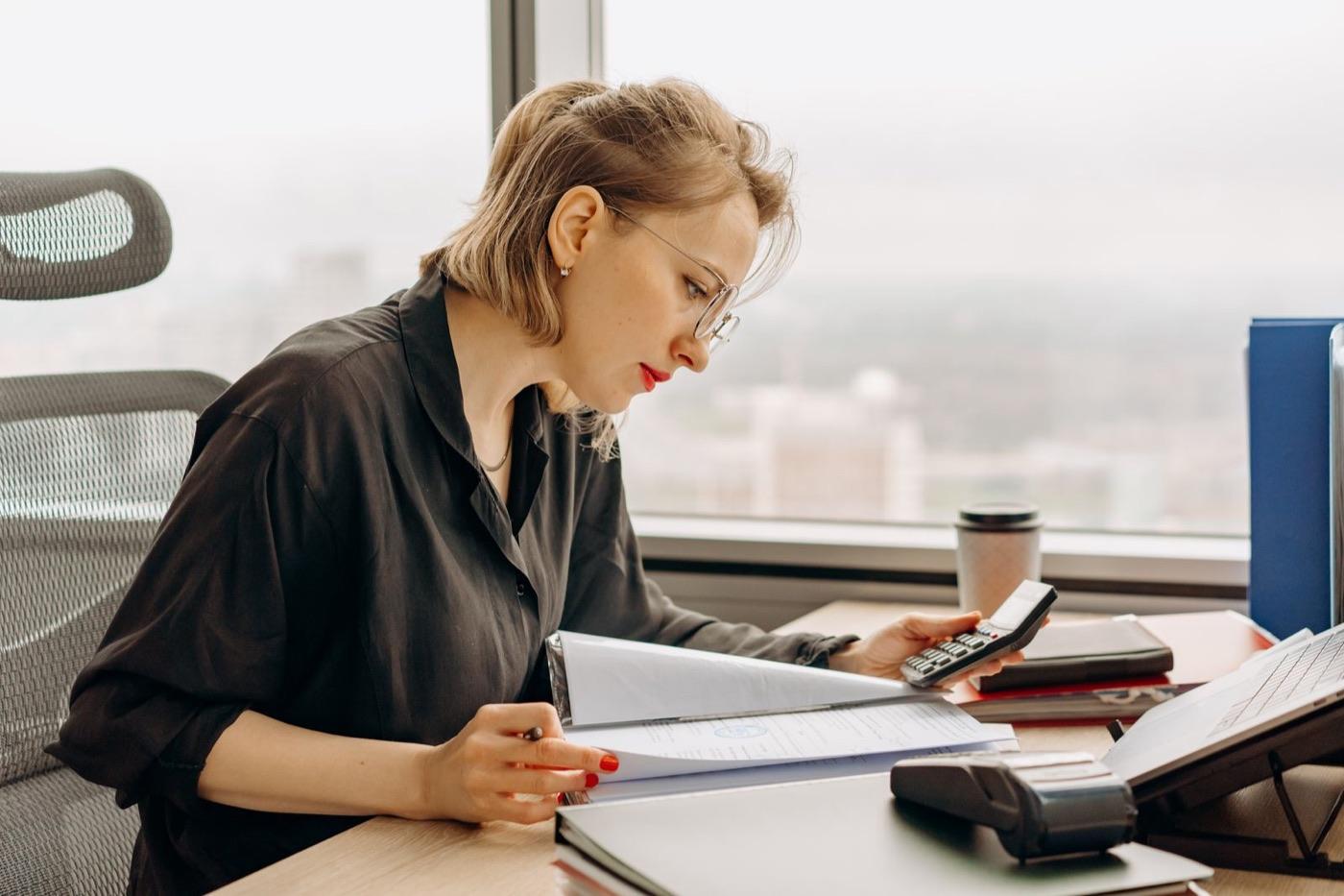Mulher fazendo contas com uma calculadora em um escritório